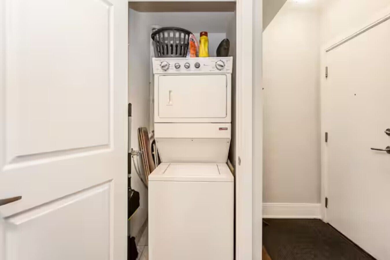 A laundry room with stacked appliances, a basket, and cleaning supplies.