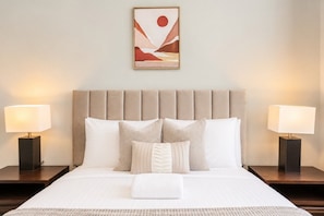 Un letto rifatto con cura, una testiera, due comodini con lampade e un'opera d'arte appesa al muro.