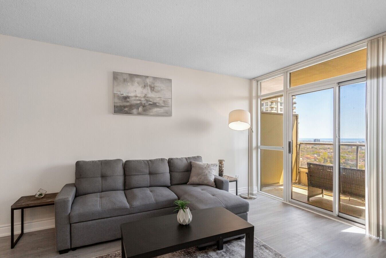 A modern living room with a grey sofa, a coffee table, a floor lamp, and a large window with a view.
