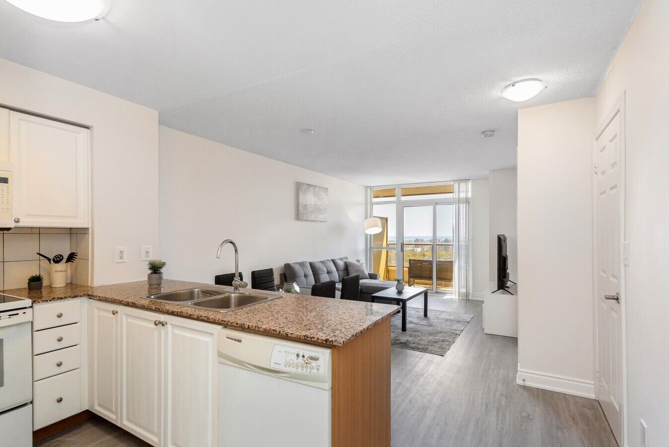 A modern kitchen with a granite countertop, stainless steel sink, and white cabinetry.
