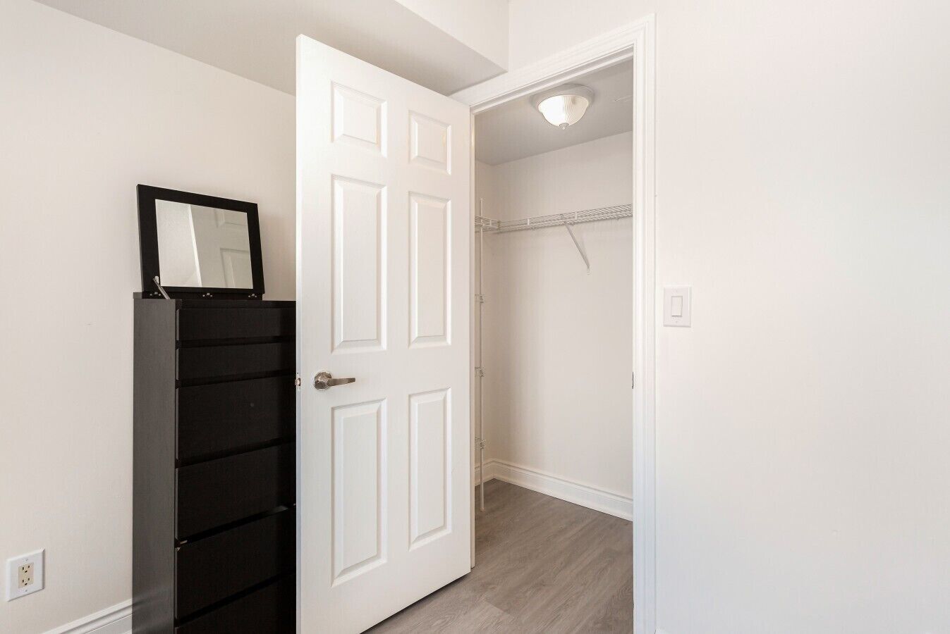 A room with a white door, a black cabinet, and a closet with a hanging rod.
