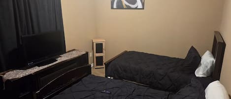 A hotel room with a bed, a TV, a small cabinet, and a painting on the wall.