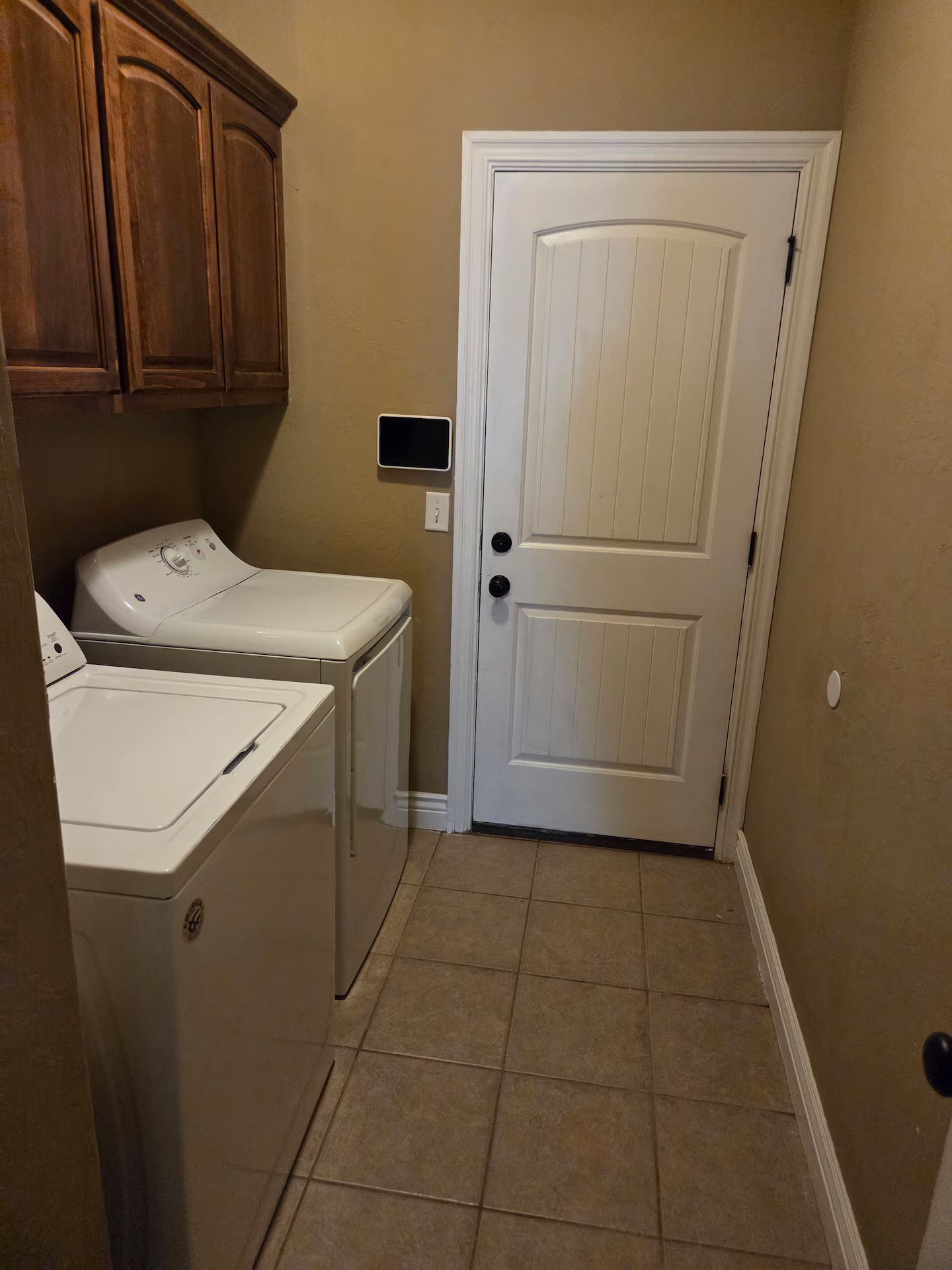 A laundry room with a white door, wooden cabinets, and two washing machines.