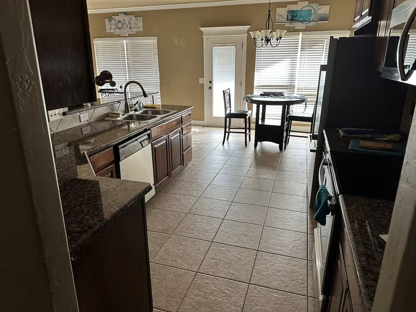 A kitchen with a dishwasher, double sink, and a dining area with a table and chairs.