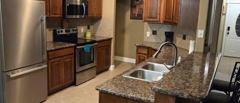 Una cocina con isla central, electrodomésticos de acero inoxidable, armarios de madera y piso de baldosas.