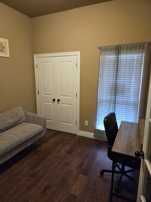 Ein Zimmer mit Holzboden, einer weißen Tür, einem grauen Sofa und einem Esstisch mit einem Stuhl.