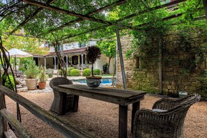 An outdoor patio with a table and chairs, surrounded by potted plants and a stone wall. - A historic 3-story estate with a pool, sleeps 10 (Fredericksburg)