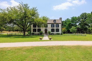 A two-story house with a symmetrical facade, a central entrance, and a gravel pathway leading to the front door. - A historic 3-story estate with a pool, sleeps 10 (Fredericksburg)