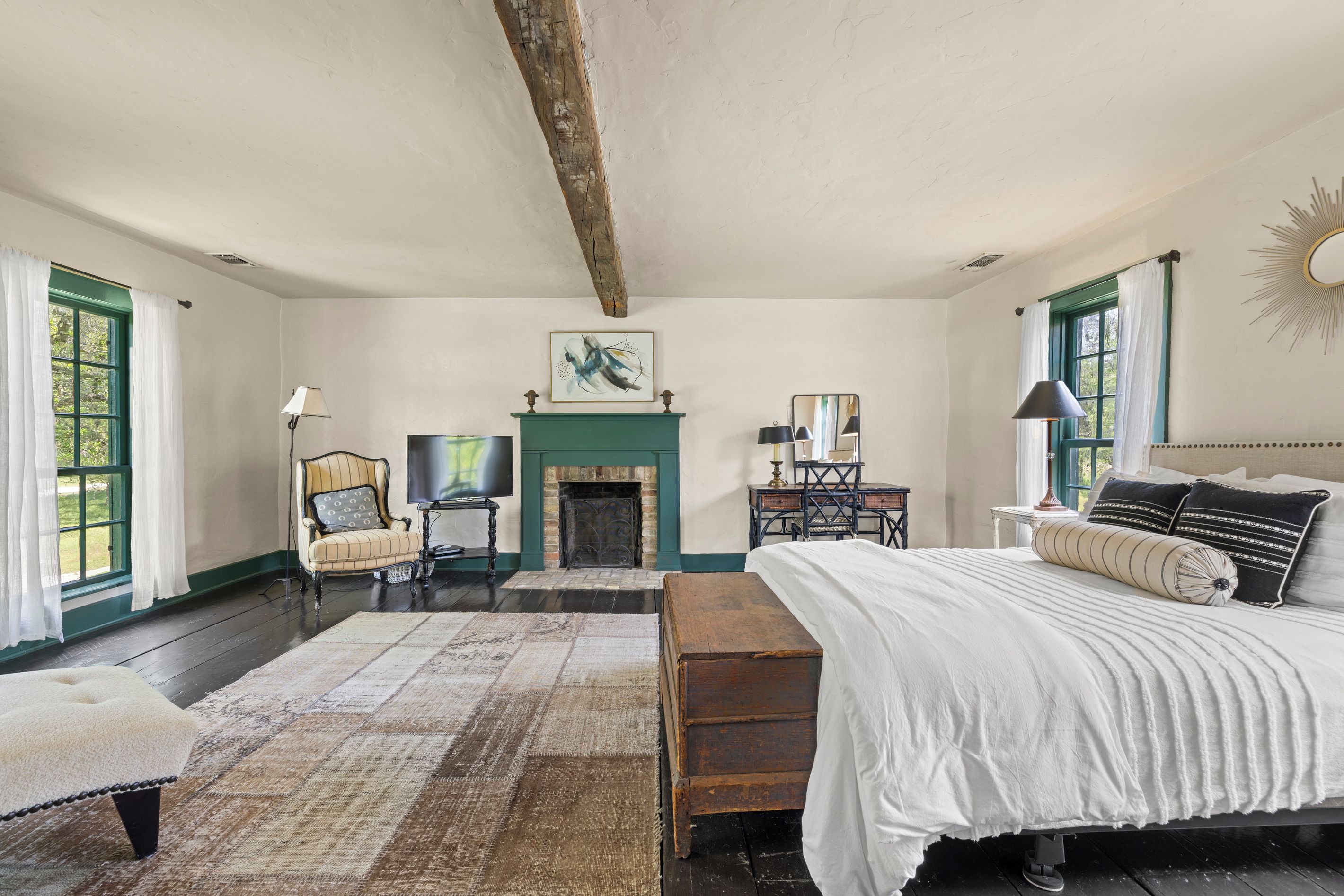 A bedroom with a large bed, a fireplace, a chair, a desk, and a window with curtains.