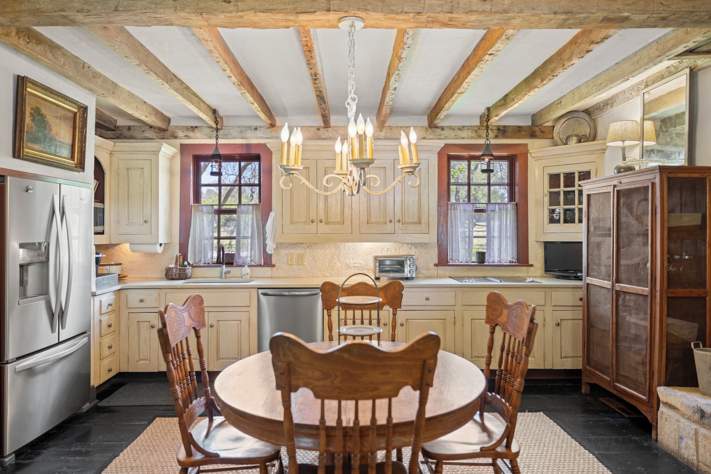A kitchen with wooden cabinets, a dining table with chairs, a refrigerator, a sink, and a chandelier.