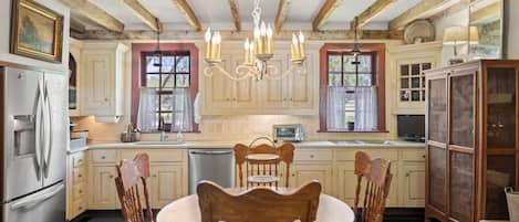 A kitchen with wooden cabinets, a dining table with chairs, a refrigerator, a sink, and a chandelier.