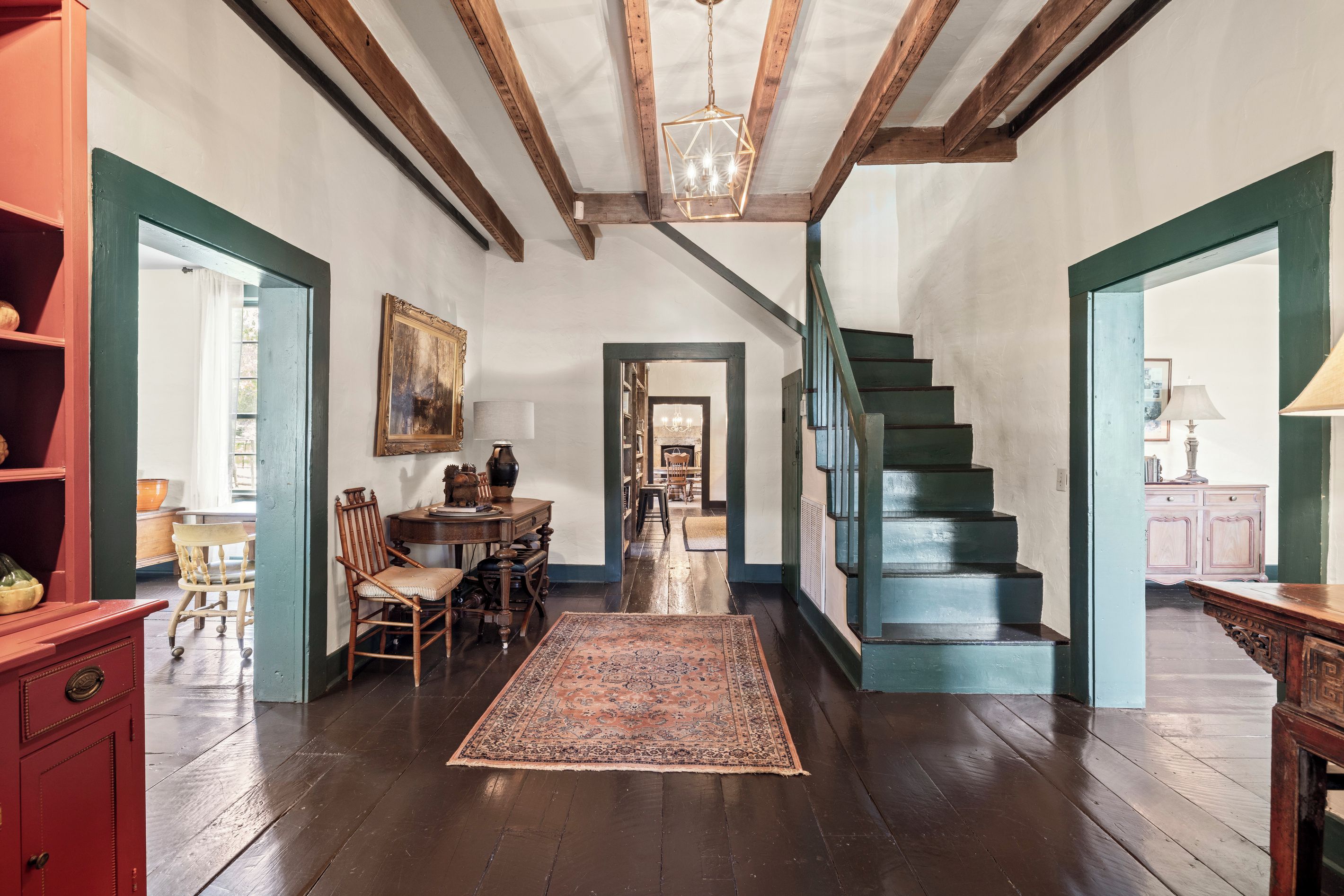 A spacious room with a wooden staircase, a dining area with a table and chairs, and a large rug on the floor.
