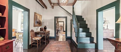 A spacious room with a wooden staircase, a dining area with a table and chairs, and a large rug on the floor.