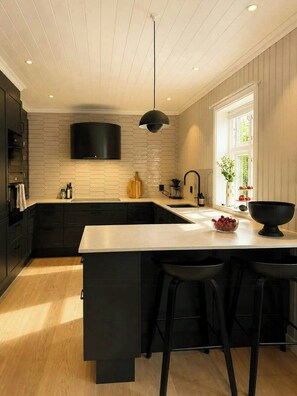 Una cocina moderna con una isla grande, taburetes negros, un televisor de pantalla plana y un ventanal que proporciona luz natural.