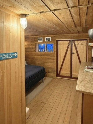Una cabaña de madera con una cama, un armario, un ventanal con imágenes y un cartel que indica el camino a la playa.