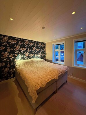 A bedroom with a large bed, floral wallpaper, and two windows.