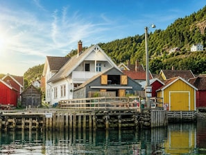 A waterfront property with a dock, a house with a balcony, and a forested hillside in the background.