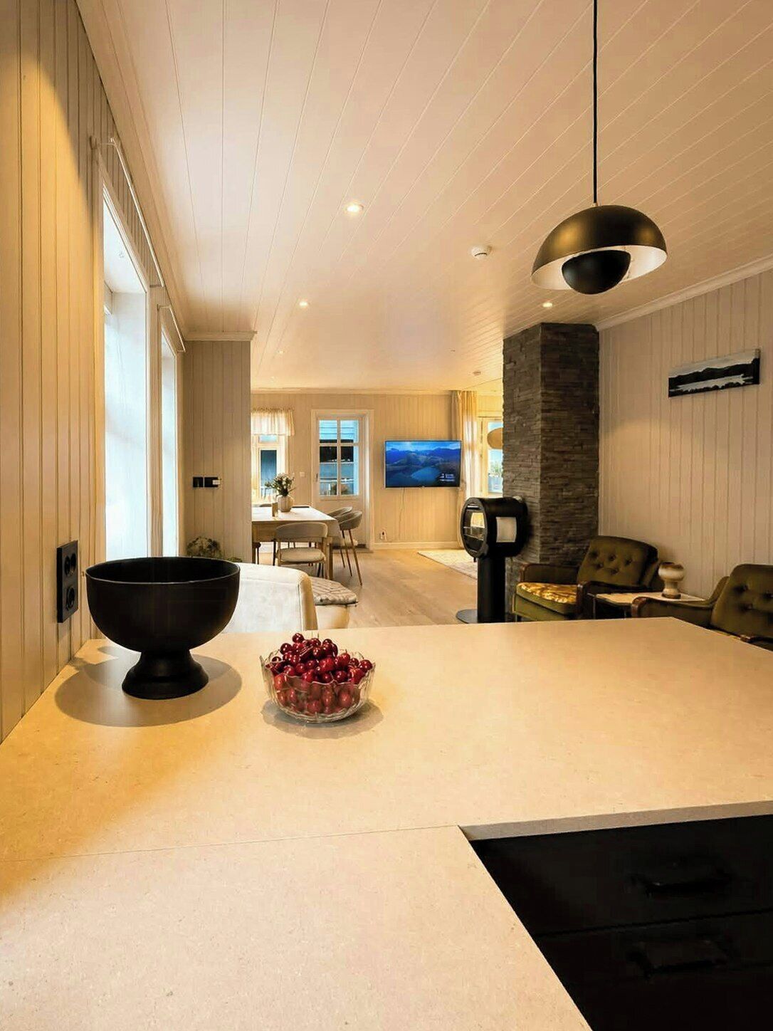 A modern kitchen with a large island, a dining area with a TV, and a stone accent wall.