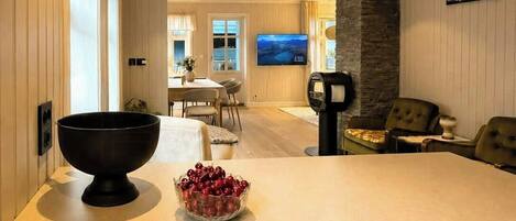A modern kitchen with a large island, a dining area with a TV, and a stone accent wall.