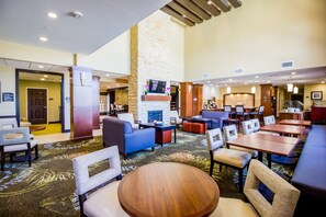 A hotel lobby with a fireplace, seating areas, and a bar. - Mobility Accessible Queen Studio | Accessible Tub (Plano)