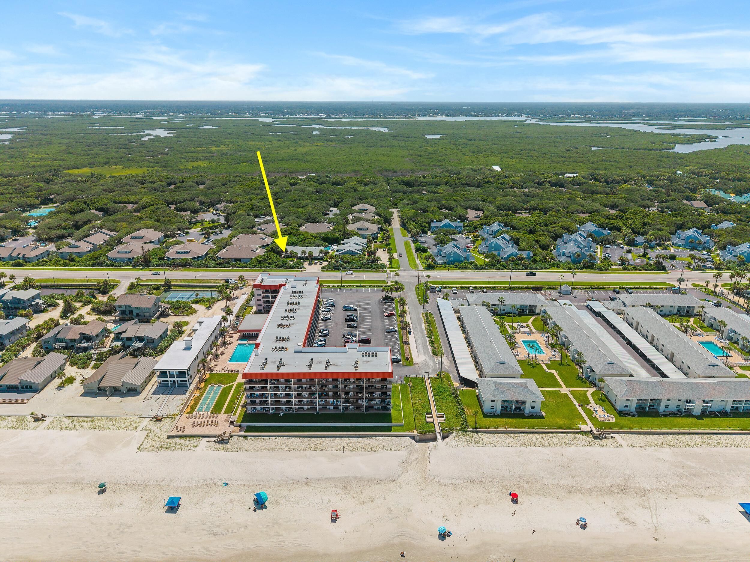 Vue aérienne d’un hôtel situé sur la côte, composé de plusieurs bâtiments, avec une plage et un port de plaisance.