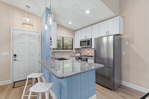 A modern kitchen with a central island, stainless steel appliances, and a blue accent wall. - Beachy Dreams NSB (New Smyrna Beach)