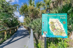 A wooden boardwalk leading through a park with a map and informational sign. - Beachy Dreams NSB (New Smyrna Beach)