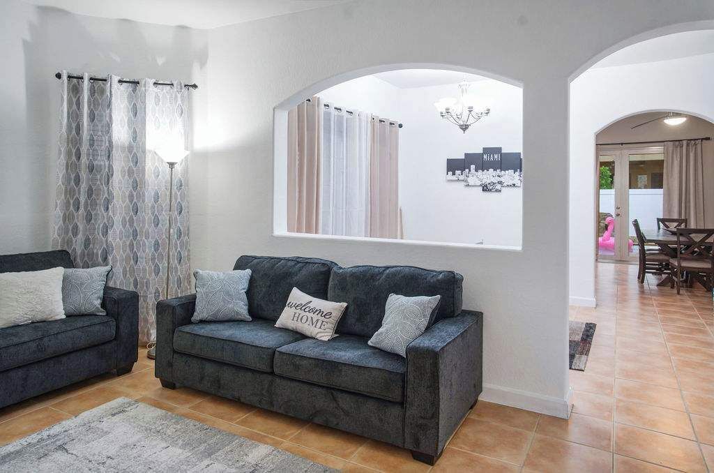 A living room with a dark grey sofa set, a patterned curtain, and a cityscape view through a window.