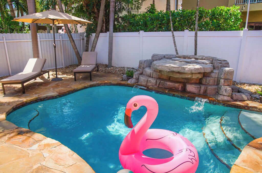Ein Schwimmbecken mit einem rosa Flamingo-Schwimmding, Liegestühlen und einer Wasserspielfeatur aus Stein.