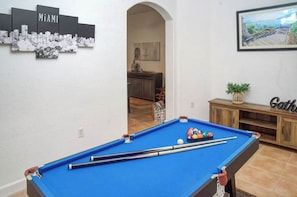A pool table with balls, a cityscape artwork, and a cabinet with a plant. - Miami Lakes Retreat Heated Pool & Kids Play Area (Hialeah)