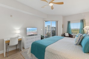 A hotel room with a bed, a desk with a television, a chair, a window with curtains, and a ceiling fan. - Oceanwalk 15-503 (New Smyrna Beach)