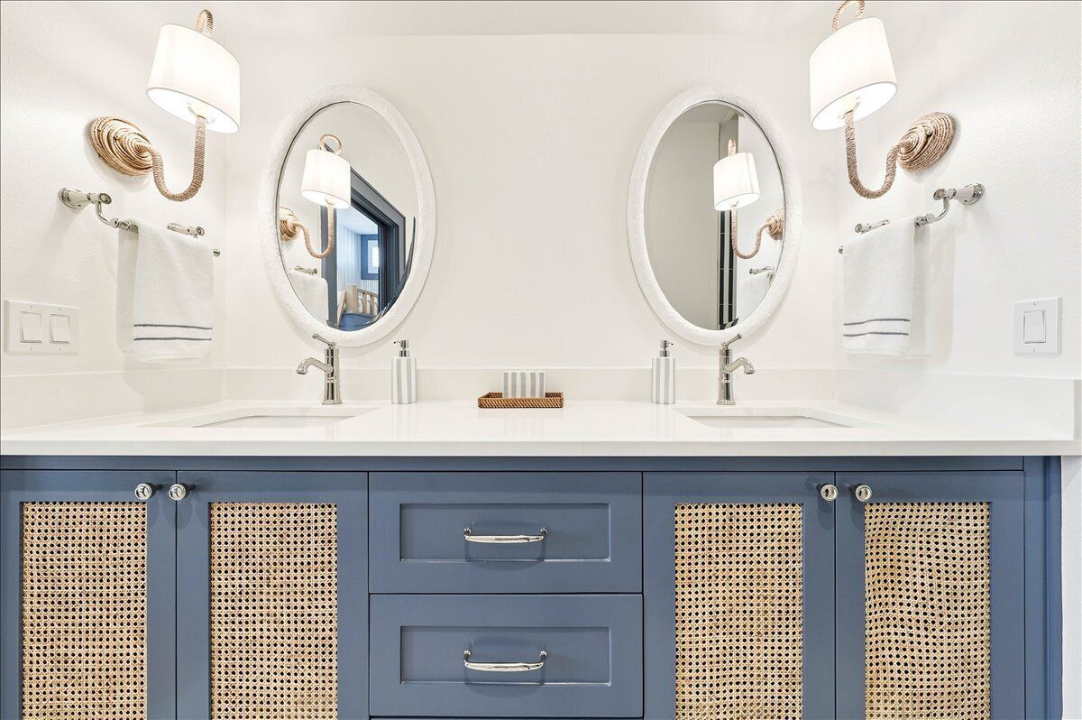 A bathroom with two sinks, each with a mirror and a wall-mounted light fixture. There are two towel racks and a small basket on the countertop.