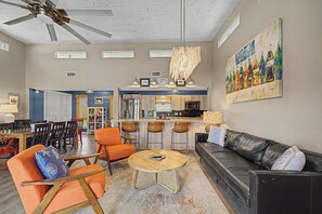 Un salon moderne avec un coin repas, une cuisine à l’arrière-plan et un ventilateur de plafond.