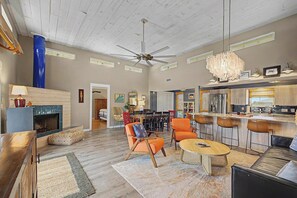 A spacious living room with a high ceiling, a fireplace, and a modern kitchen with a bar area. - 1112 Maldonado-Tropic Like Its Hot (Pensacola Beach)