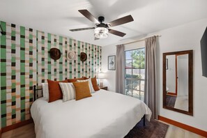 Une chambre d’hôtel avec un grand lit, un ventilateur de plafond, une fenêtre avec des rideaux et un mur orné d’un motif géométrique.