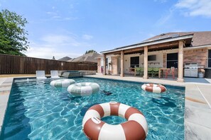 A swimming pool with inflatable rings, a covered patio area, and a barbecue grill. - Hachie Hangout | Pool, Hot Tub, Pool Table, Fire Pit & Games (Waxahachie)