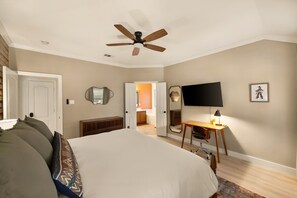 A bedroom with a bed, a desk, a chair, a ceiling fan, a TV, and a door leading to another room. - Hachie Hangout | Pool, Hot Tub, Pool Table, Fire Pit & Games (Waxahachie)