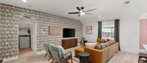 Una sala de estar moderna con un sofá, una silla, un televisor y un ventilador de techo.