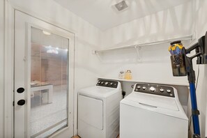 A laundry room with two washing machines, a dryer, and a blue vacuum cleaner. - Hachie Hangout | Pool, Hot Tub, Pool Table, Fire Pit & Games (Waxahachie)