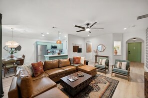 A modern living room with a sectional sofa, a coffee table, and a dining area with a chandelier. - Hachie Hangout | Pool, Hot Tub, Pool Table, Fire Pit & Games (Waxahachie)