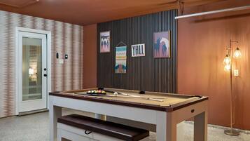 A pool table with balls, a door, and wall decorations in a room with a patterned wall and a light fixture.