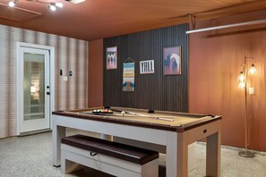 A pool table with balls, a door, and wall decorations in a room with a patterned wall and a light fixture. - Hachie Hangout | Pool, Hot Tub, Pool Table, Fire Pit & Games (Waxahachie)
