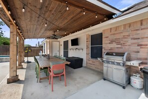 An outdoor patio with a wooden pergola, a barbecue grill, and a dining table with chairs. - Hachie Hangout | Pool, Hot Tub, Pool Table, Fire Pit & Games (Waxahachie)