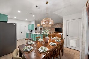 A modern kitchen with teal cabinets, a dining area with a wooden table set for four, and a hanging light fixture. - Hachie Hangout | Pool, Hot Tub, Pool Table, Fire Pit & Games (Waxahachie)