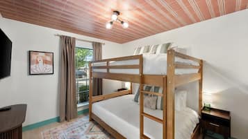 A bunk bed room with a ceiling fan, a window with curtains, a framed picture on the wall, and a small bedside table with a lamp.