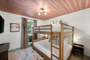 A bunk bed room with a ceiling fan, a window with curtains, a framed picture on the wall, and a small bedside table with a lamp. - Hachie Hangout | Pool, Hot Tub, Pool Table, Fire Pit & Games (Waxahachie)