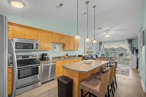 A modern kitchen with stainless steel appliances, wooden cabinets, and a central island with bar stools. - Escape by the bay! Baywatch E10 (Pensacola Beach)