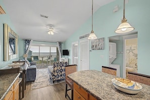 A spacious kitchen with granite countertops, a dining area with chairs, and a view of the sea through large windows. - Escape by the bay! Baywatch E10 (Pensacola Beach)