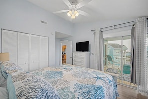 A bedroom with a bed, a ceiling fan, a TV, and a sliding glass door to a balcony. - Escape by the bay! Baywatch E10 (Pensacola Beach)