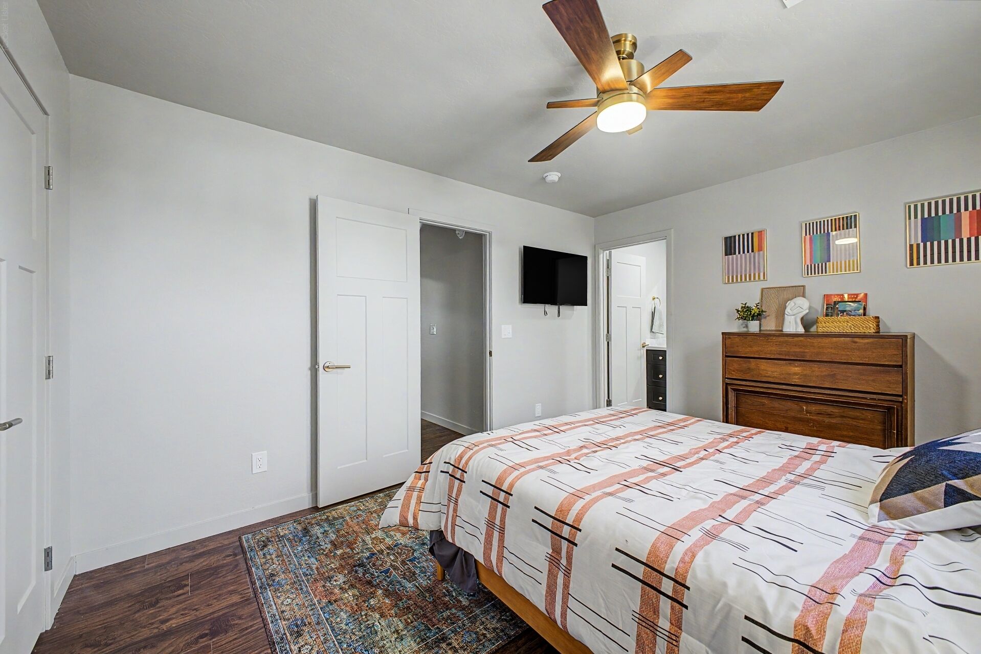 Un dormitorio con cama, ventilador de techo, televisor, cómoda y alfombra.